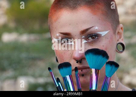 Portrait de visage d'une jeune belle femme avec un maquillage de fantaisie et des pinceaux de maquillage colorés couvrant son visage. Banque D'Images