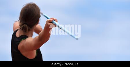 Une athlète féminine lance un javelin sur un terrain d'herbe pendant une course et un campeur de terrain, vue arrière Banque D'Images