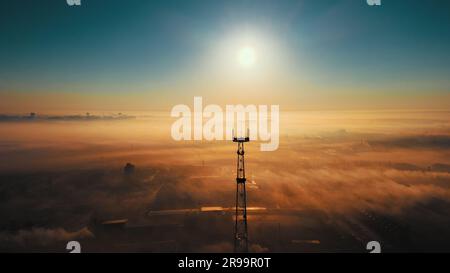 Paysage de drone. Soleil sur la ligne d'horizon et brouillard sur la zone industrielle. Tour de communication contre le ciel. Belle aube. Banque D'Images