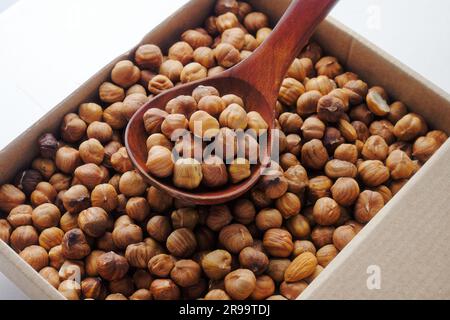 Boîte de noisettes pelées. Vue de dessus. Livraison de noix saines dans une boîte en carton. Un tas de noisettes dans une cuillère en bois. Banque D'Images