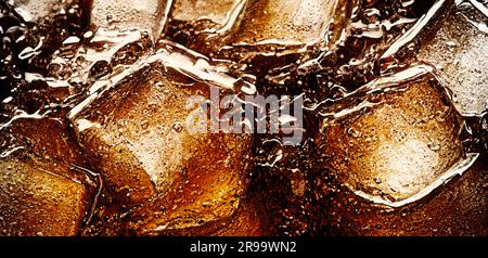 Cola avec glace. Gros plan des glaçons dans l'eau de cola. Texture de la boisson carbonate avec bulles dans le verre. Soda et glace éclaboussant ou flottant Banque D'Images