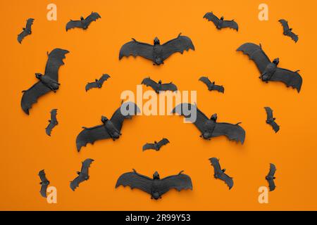 Beaucoup de chauves-souris noires volent sur un fond orange. Banque D'Images