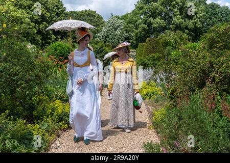 Femmes vêtues de robes victoriennes vintage ou de costumes marchant dans un jardin anglais en été portant des parasols, Angleterre, Royaume-Uni Banque D'Images