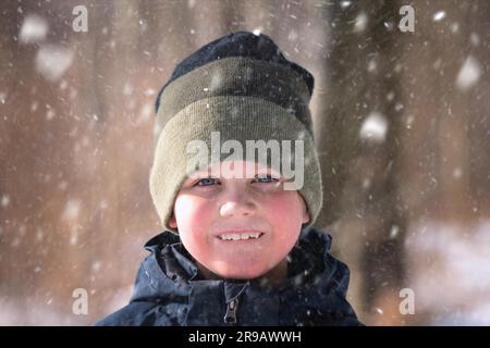 Jeune garçon dans la neige avec un bonnet tricoté et un joli sourire sur son visage en profitant de l'extérieur Banque D'Images