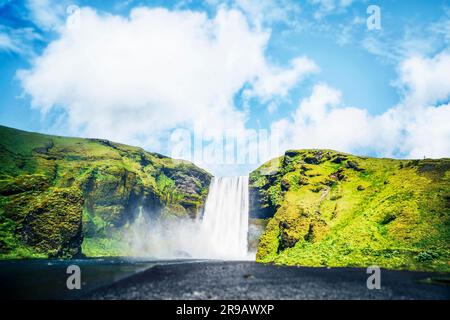 Cascade entre falaises vertes sous un ciel bleu en Islande Banque D'Images