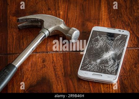 L'écran du téléphone fracassé sur une table avec un marteau Banque D'Images