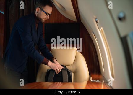 Gros plan élégant homme d'affaires sort un ordinateur portable moderne et le place sur la table pour travailler dans le jet privé d'avion de première classe Banque D'Images