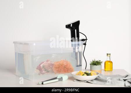 Circulateur à immersion thermique et viande emballée sous vide dans une boîte sur une table en bois blanc. Cuisson sous vide Banque D'Images
