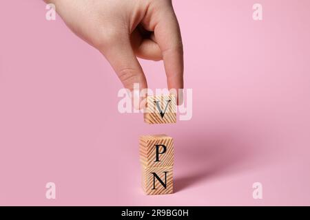 Femme faisant l'acronyme VPN avec des cubes en bois sur fond rose pâle, gros plan Banque D'Images