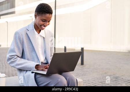 portrait horizontal d'une jeune femme africaine élégante. Elle est assise près du tribunal et utilise un ordinateur portable Banque D'Images