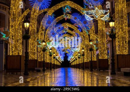 Carnaval avec lumières décoratives de Noël en Espagne. Les lumières se reflètent dans la rue de la ville la nuit. Le masque de Carnaval est similaire à un masque Mardi gras. Banque D'Images