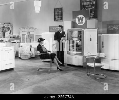 États-Unis: 1939 Un vendeur présente les mérites des réfrigérateurs Westinghouse à une femme dans une salle d'exposition d'appareils Westinghouse. Banque D'Images