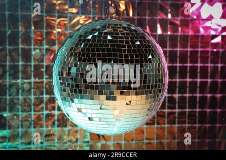 Boule disco brillante contre le rideau de fête en aluminium sous la lumière rose et turquoise Banque D'Images