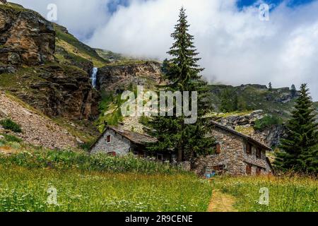 Vue sur le champ rural, deux maisons en pierre et la montagne avec petite cascade en arrière-plan en Italie. Banque D'Images