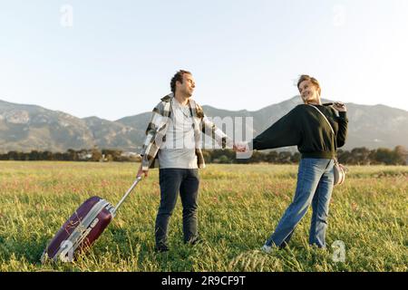 Un jeune couple épris inspiré regarde le plan de vie à l'avenir. Ils sont debout avec une valise et ukulele, tenant les mains. Recherche d'une nouvelle patrie. Banque D'Images