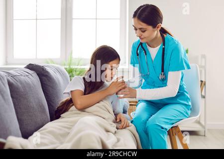 Femme médecin rend visite à une fille malade, l'aide à prendre des médicaments et donne son verre d'eau Banque D'Images