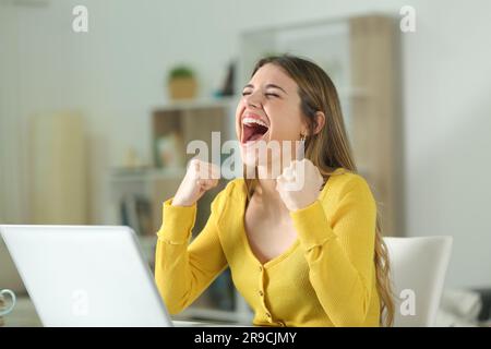 Femme excitée avec un ordinateur portable célébrant la réussite à la maison Banque D'Images