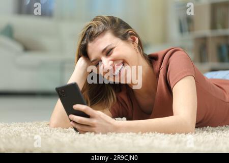 Bonne femme regardant des vidéos sur un téléphone couché sur un tapis à la maison Banque D'Images