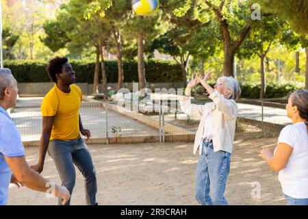 Club social de joyeux personnes âgées diverses appréciant le volley-ball le jour ensoleillé d'octobre plein air Banque D'Images