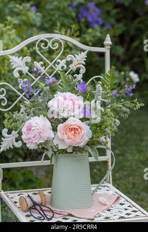 bouquet de roses, pivoines et fleurs d'été en carafe vintage sur chaise de jardin Banque D'Images