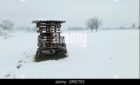 Pile de vieilles palettes en bois usagées sur le dessus de quatre blocs de construction rouges recouverts de grande tuile de toit et la neige laissée dans le champ local couvert avec Banque D'Images