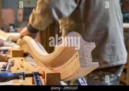 Charpentier sable cintrage garde-corps en bois avec papier de verre en atelier de clôture. Maître senior fait le détail de l'escalier en colimaçon pour l'intérieur de la maison Banque D'Images