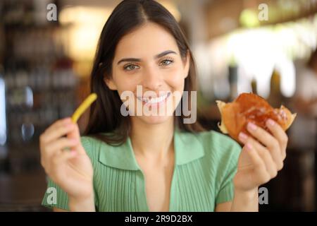 Un client satisfait du restaurant qui tient des pommes de terre et des sandwichs vous regarde Banque D'Images