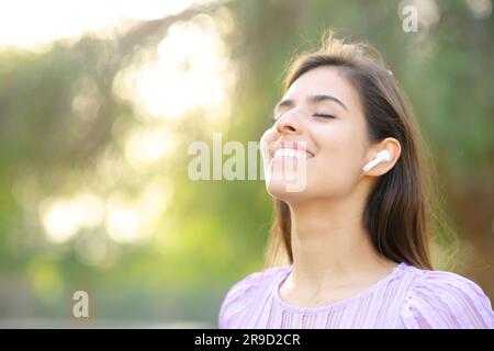 Une femme heureuse respire de l'air frais en portant un écouteur dans un parc vert Banque D'Images