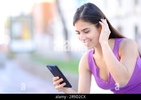 Bonne femme utilisant le téléphone touchant les cheveux dans la rue Banque D'Images