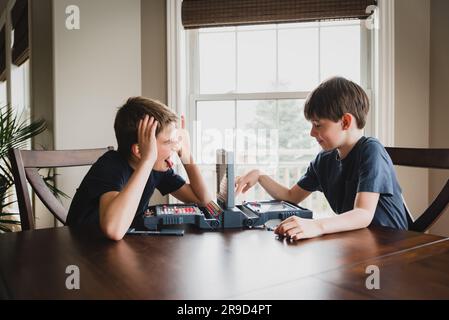 Garçon faisant des visages à son frère comme ils jouent un jeu de société ensemble. Banque D'Images