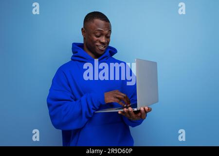 superbe pigiste américain à la peau sombre de 25 ans, dans un élégant sweat à capuche avec ordinateur portable en arrière-plan et espace de copie Banque D'Images