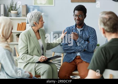 Un jeune Africain américain décrivant son problème psychologique au conseiller et à d'autres patients bien sûr en étant assis devant eux Banque D'Images