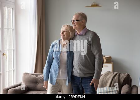 Une femme et un mari âgés souriants qui s'embrasse donnent sur la fenêtre Banque D'Images