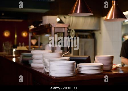 Plusieurs piles de plaques blanches sur le comptoir ou sur le lieu de travail du chef entouré d'équipements de cuisine et de lampes suspendues au-dessus Banque D'Images