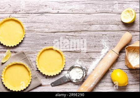 Pâte crue dans des casseroles, un rouleau à pâtisserie avec de la farine, un zeste de citron et un citron entier, sur un fond en bois avec espace de copie. Recette de tarte au citron. Banque D'Images