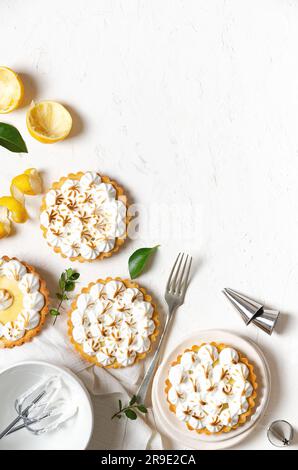 Mini tartes au citron avec meringue, zeste de citron, feuilles de citron, fouets avec meringue, une fourchette, et quelques buses de tuyauterie, sur un fond blanc avec espace de copie. Banque D'Images