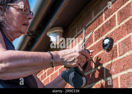 Femme fixant la lumière extérieure avec une infrarouge infrarouge sur le mur extérieur d'une maison. Banque D'Images