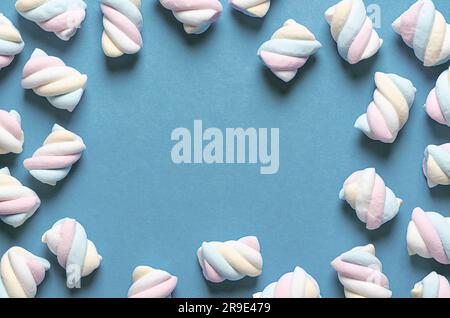 Guimauves blanches, jaunes, roses et bleu clair sur fond bleu avec espace de copie. Banque D'Images