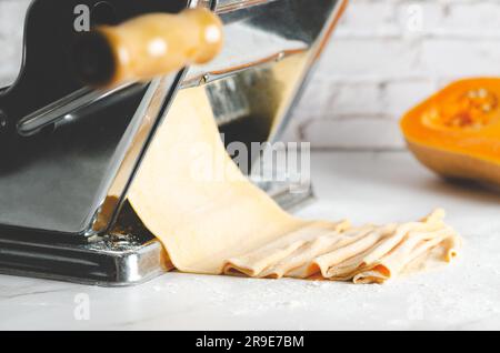 Pâte de courge butternut dans une machine à pâtes, et un morceau de courge butternut, sur fond de marbre. Banque D'Images