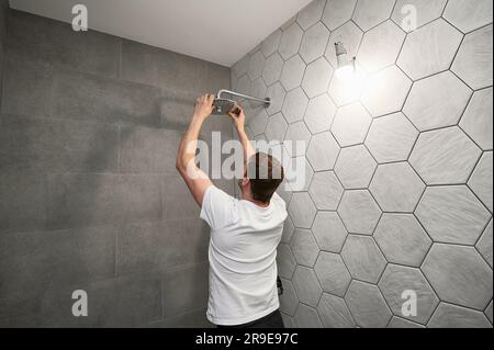 Homme travaillant à réparer la pomme de douche de la salle de bains tout en travaillant à la rénovation de la salle de bains. Vue arrière de l'homme plombier installation de la pomme de douche de bain haute pression à la maison. Banque D'Images