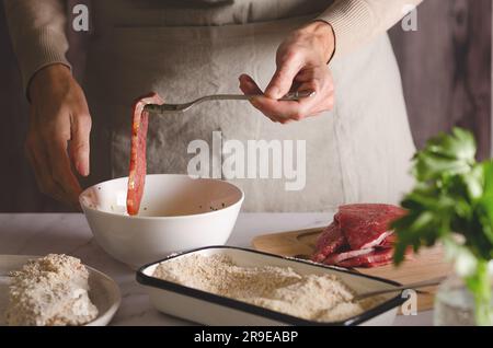 Gros plan des mains féminines cuisinant des milanesas argentines dans la cuisine à la maison. Banque D'Images