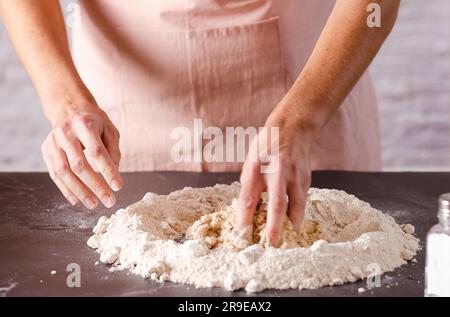 Mains féminines pétrissant la pâte dans la cuisine, gros plan. Procédé de cuisson. Banque D'Images