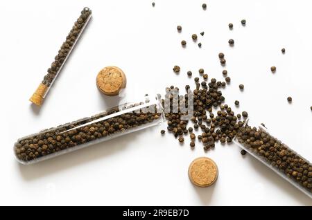 Grains de poivre noir dans des récipients en verre et liège sur fond blanc. Banque D'Images