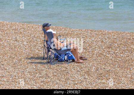 Un couple bronzer dans des chaises de plage bleues sur une plage de galets Banque D'Images