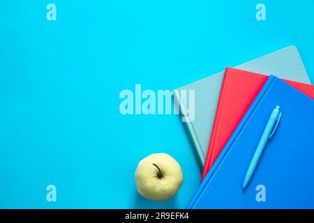 Blocs-notes multicolores et pomme sur fond bleu, vue de dessus. Banque D'Images