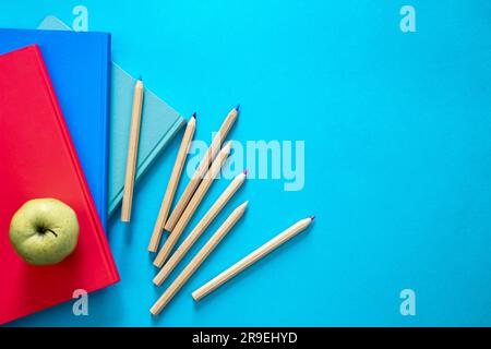 Carnets, pomme et crayons sur fond bleu, vue du dessus. Banque D'Images