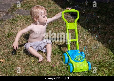 Un petit garçon pousse une tondeuse qui souffle des bulles dans le jardin Banque D'Images