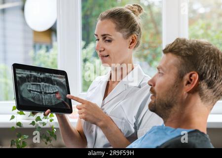 dentiste montrant et expliquant à son patient une photo de radiographie dentaire avec une dent de sagesse affectée Banque D'Images