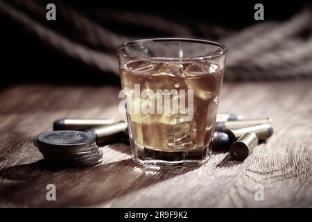 Whisky tiré avec glace et munitions avec pièces de monnaie anciennes en argent sur une table de bar en bois Banque D'Images