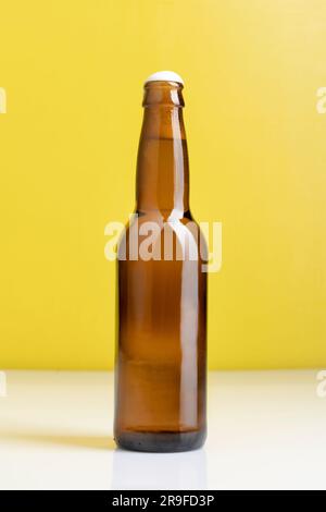 Une bouteille de bière brune debout sur une table blanche sur fond jaune Banque D'Images